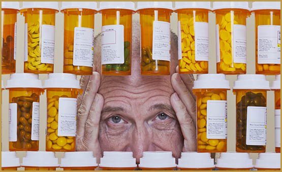 Senior man with an unhappy, depressed expression and his hands framing his face looking through an opening in rows of prescription medication. Health care and medication cost can overwhelm many senior citizens.