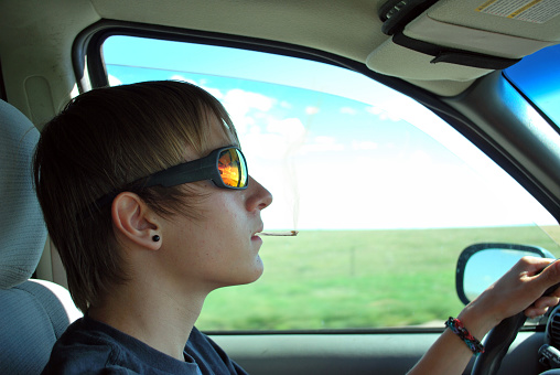 a teenage boy smoking a marijuana joint while driving.